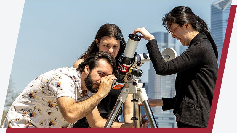 Students look through a telescope with their professor.