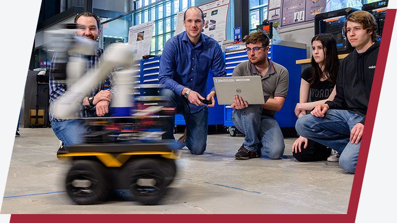 Students control a wheeled robot arm using a laptop in the lab