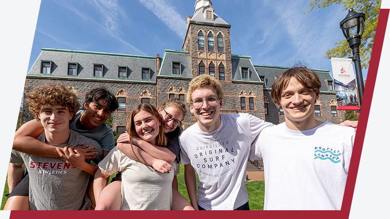 A group of six students smile for the camera in front of the EAS building on Stevens campus.
