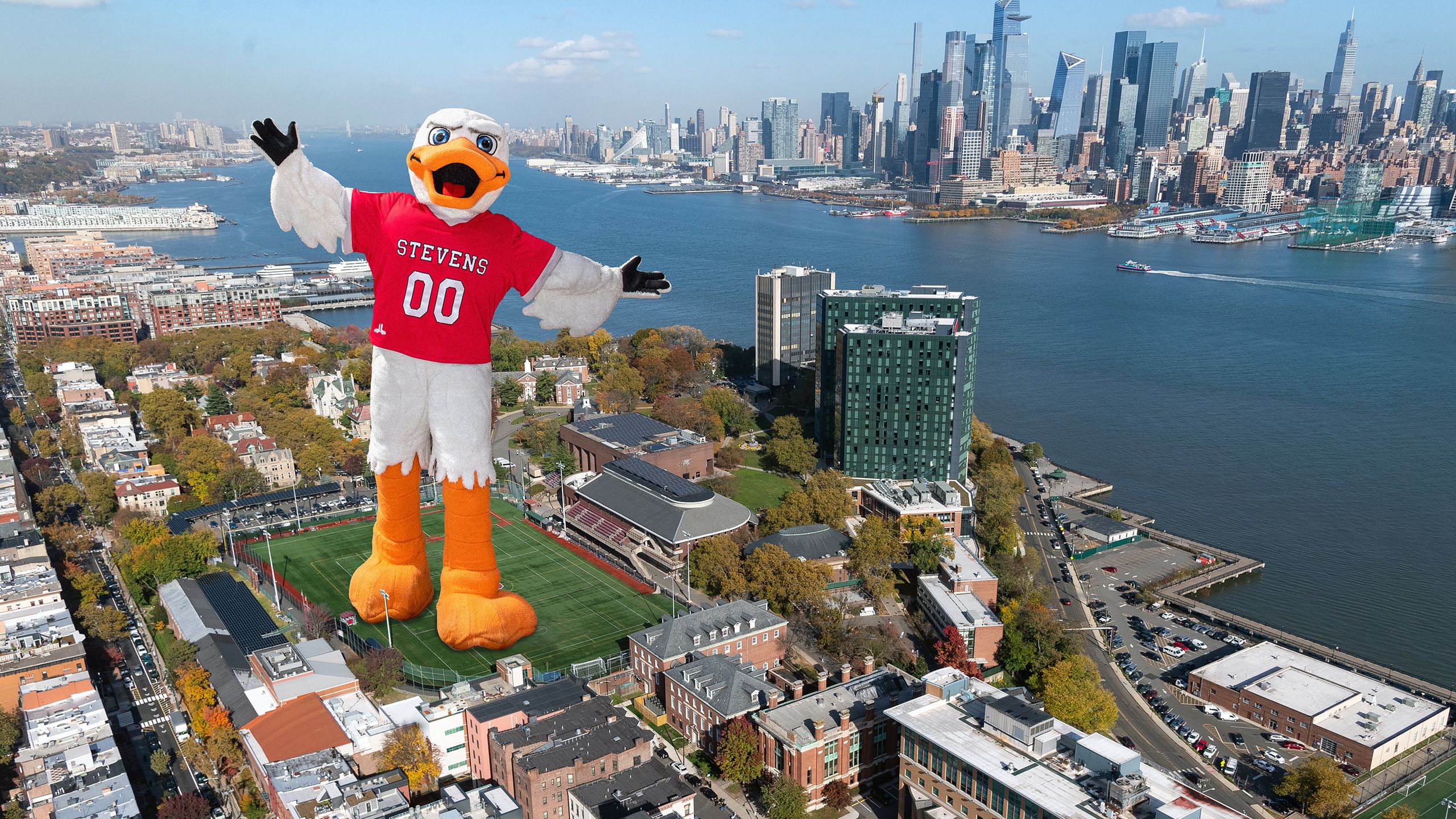 Giant Attila the duck mascot stands on Stevens campus with New York city skyline in background.
