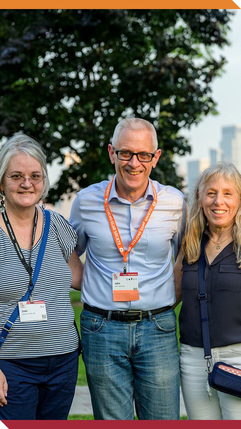 Three alumni smile on campus in front of the New York skyline.