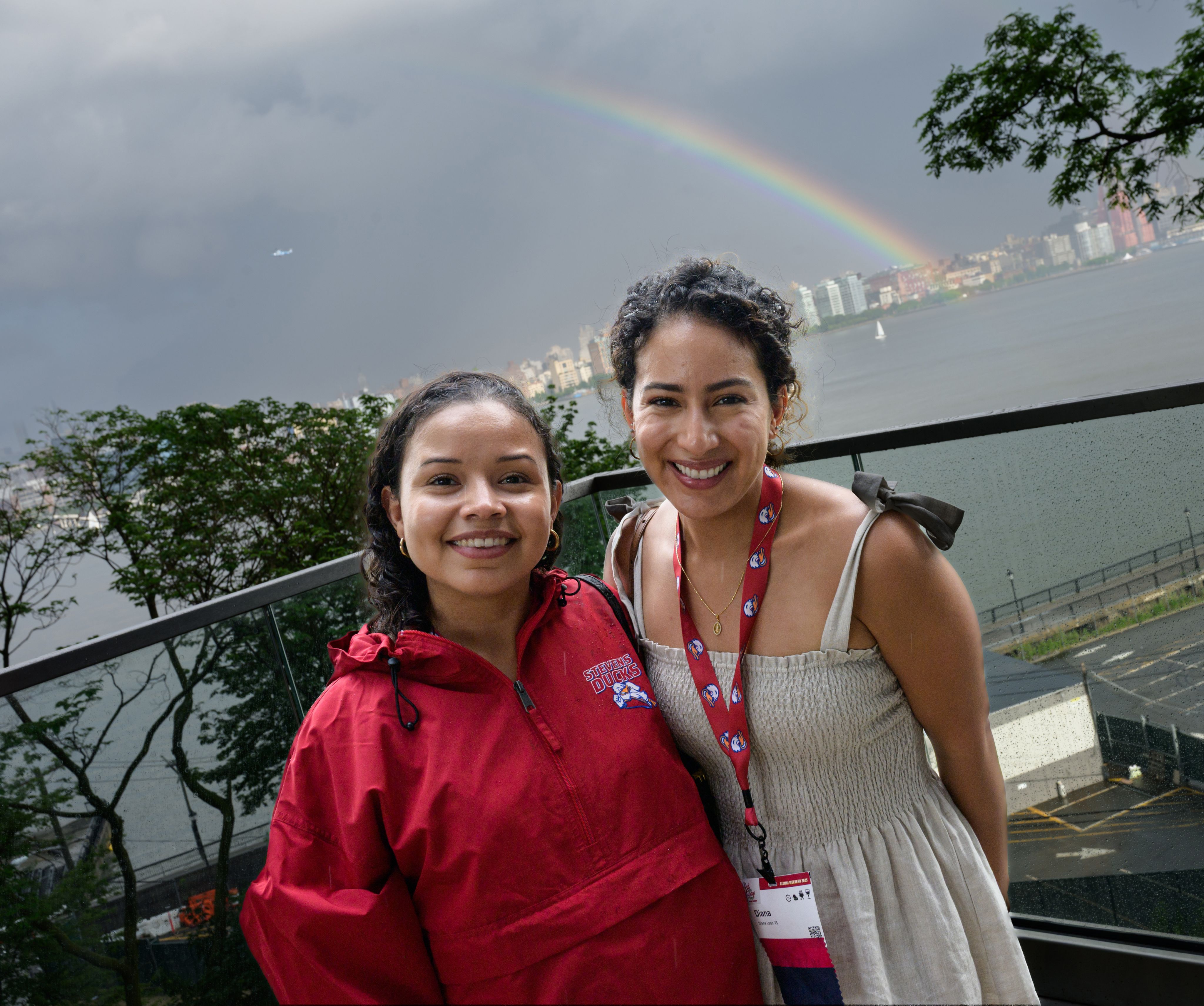 Two Stevens alumni on campus with a rainbow behind them over the New York skyline.